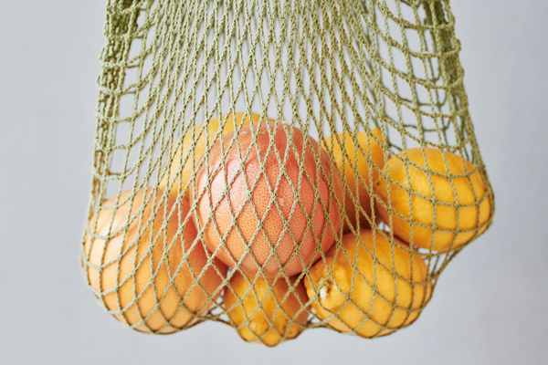 Green organic string bag filled with citrus fruits against a light background