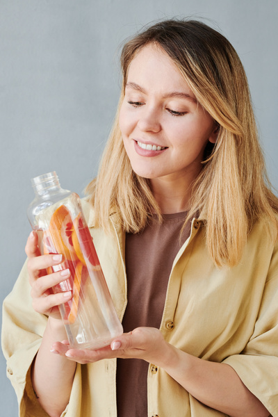 A blonde woman in a beige shirt smiling looks at a transparent bottle of grapefruit drink in her hands