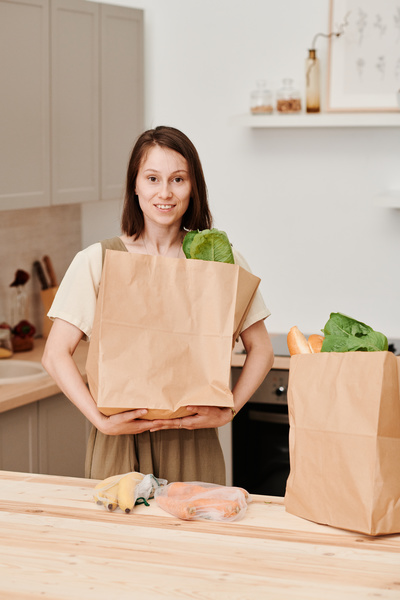 A woman with dark short hair standing in the kitchen holding an eco-friendly paper shopping bag