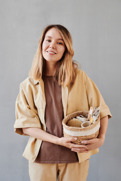 A woman with blonde hair dressed in a beige outfit with a wicker eco basket of toiletries
