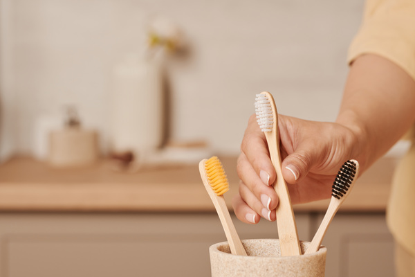 A woman taking an environmentally friendly toothbrush from a light-colored toothbrush holder
