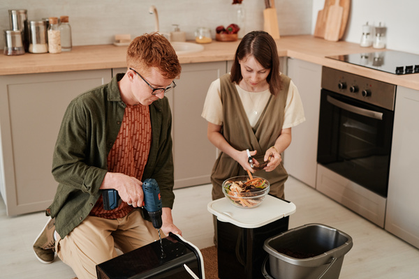 A man with reddish hair kneeling in the kitchen with a woman with dark hair preparing black plastic containers for organic fertilizer