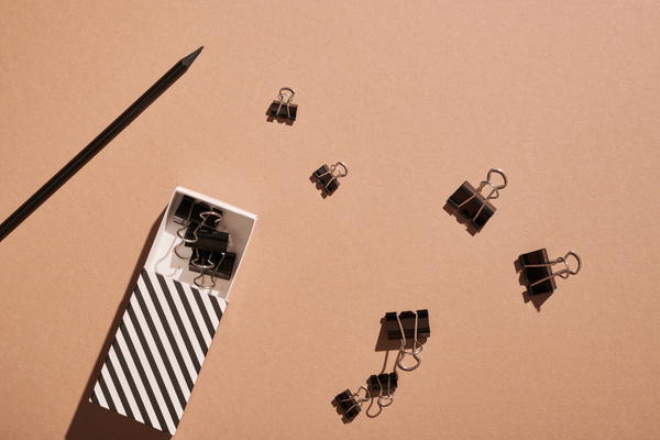 Black binder clips of various sizes scattered around a striped case for them next to a black pencil