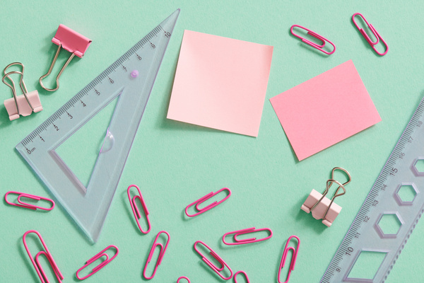 Top view of bright pink office supplies scattered on a turquoise surface