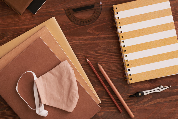 Top view of brown notepads and a striped spiral notebook lying on a table with stylish writing materials and a reusable medical mask