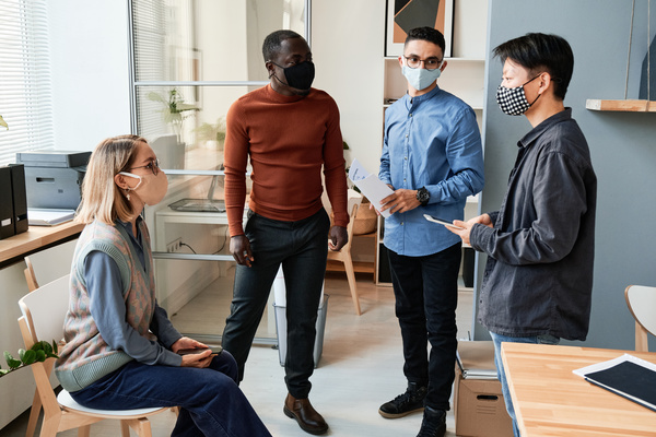 Office workers in reusable medical masks discussing a project in a bright office