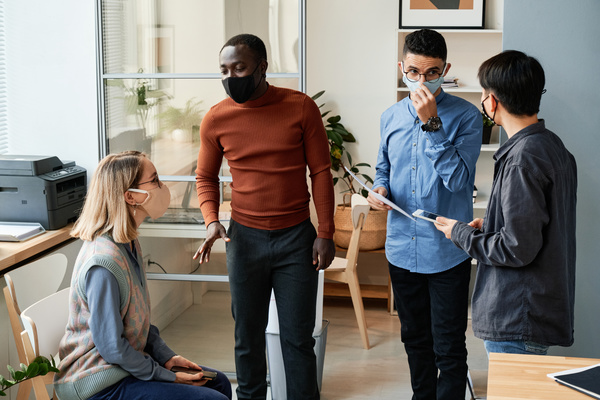 Office workers in reusable face masks communicating with each other in a bright office