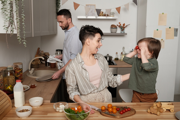A woman with dark short hair having fun with her little son in pajamas while cooking a vegetable salad in the kitchen
