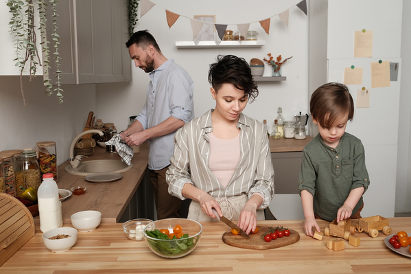A woman with dark short hair cooking a vegetable salad and her son playing with wooden toys