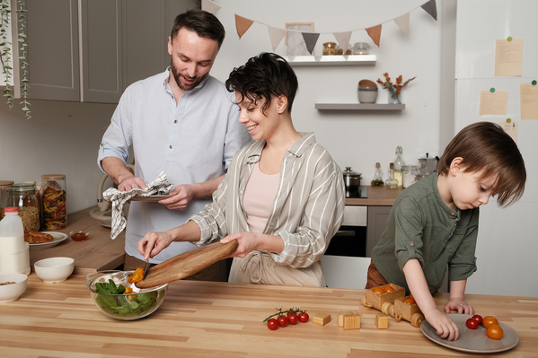 A smiling family consisting of young parents and their son cooking vegetable salad in the kitchen