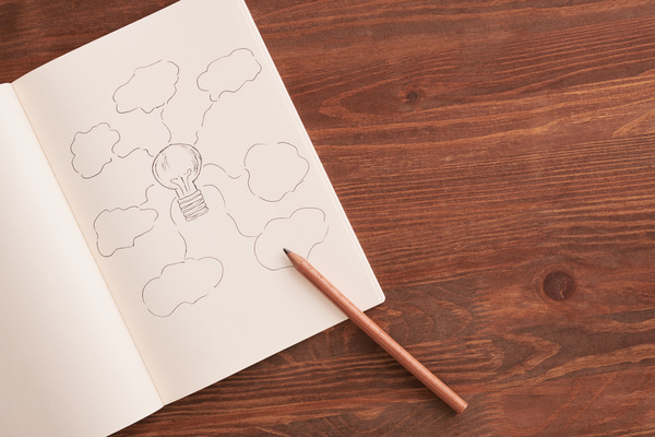 A notebook with a drawing symbolizing ideas and a pencil on a wooden table