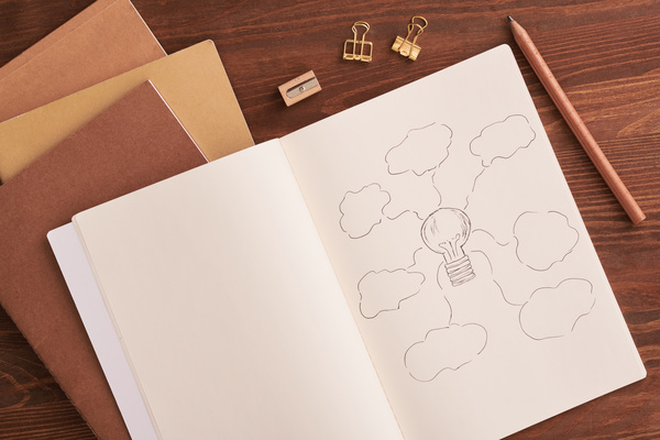 A notepad with a drawing symbolizing ideas and a pencil lying on a wooden desk with a stationery