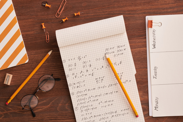 Top view of math notes in a notebook lying on a table with an orange office supplies and glasses with round lenses