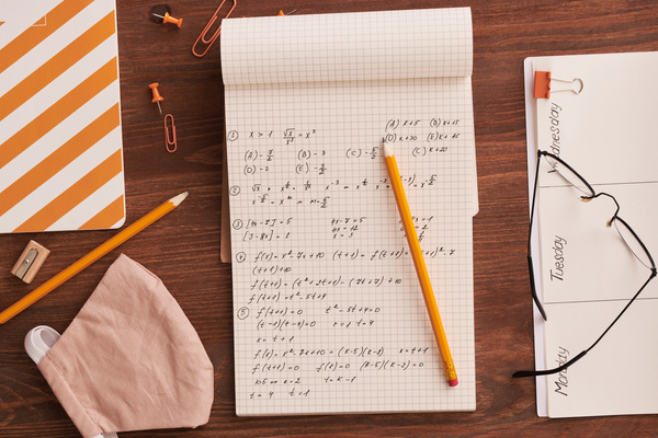 Top view of the mathematics notes in a notepad lying on a table with an orange office and a reusable medical mask