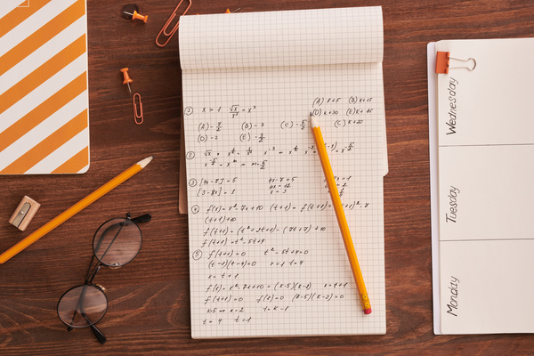 A notebook with written mathematical calculations lying on a table with a yellow office and glasses