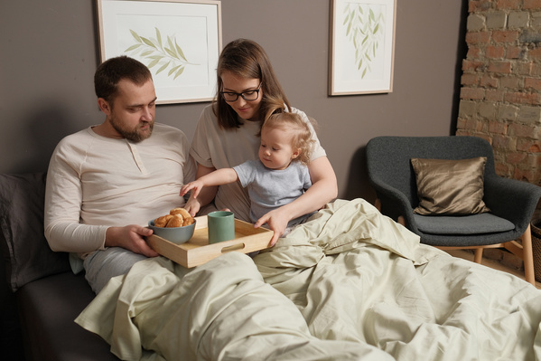 Family members in light pajamas sitting in bed with breakfast on a wooden tray