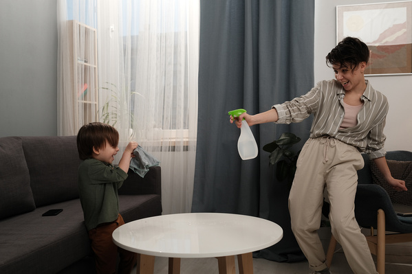 A woman with short hair having fun with her little son during home cleaning