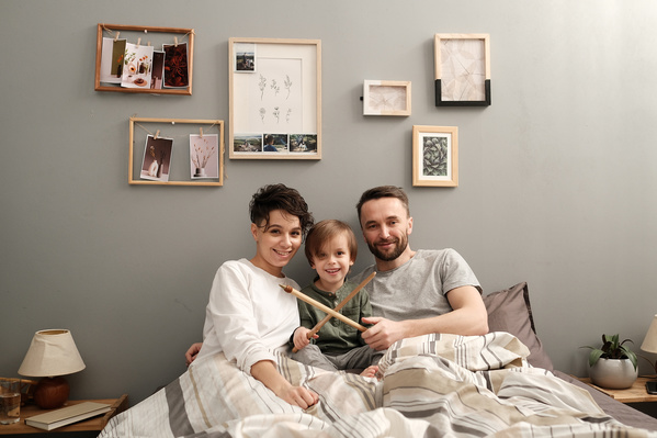 Smiling dark-haired parents in pajamas and their son with toy arrows sitting in bed