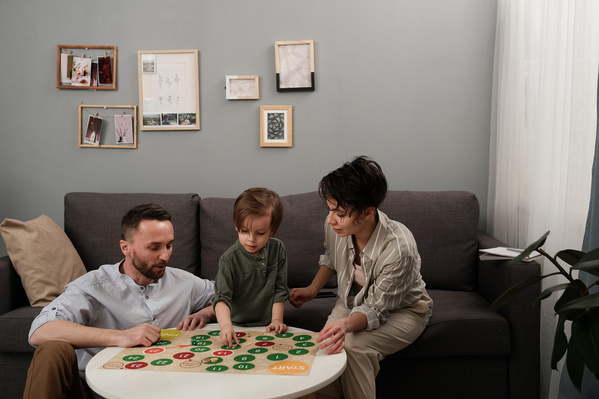 Dark-haired parents dressed in light clothes playing a board game with their little fair-haired son at home
