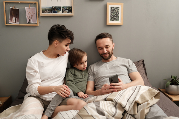 A family consisting of parents and their child using the phone while sitting in bed