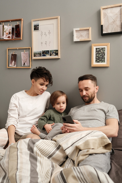 A family consisting of parents and their son watching cartoons on the phone while sitting in bed