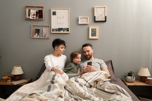 A family consisting of parents and their son playing a game on the phone while sitting in bed