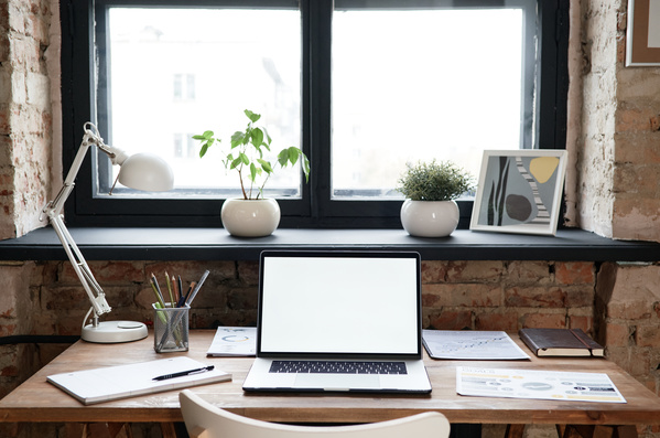 Laptop and stationery on a wooden work desk at the window with indoor plants