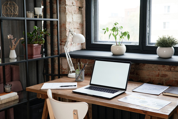 Wooden desk with laptop and writing materials in a loft-style office