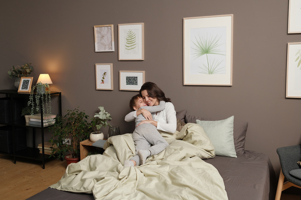 A woman in light clothes cuddling with her little son wearing pajamas in bed