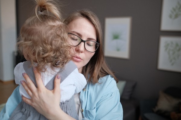 A woman in glasses and a blue shirt hugging her little blonde daughter