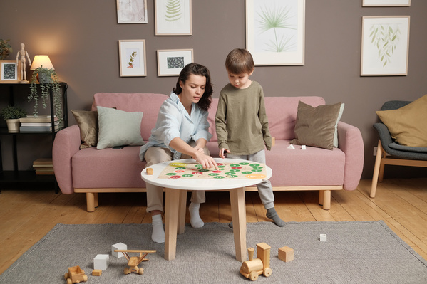 Dark-haired mom in light clothes playing a board game with her little son in pajamas