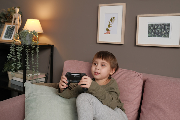 A little boy with brown hair dressed in pajamas playing a video game with a black joystick