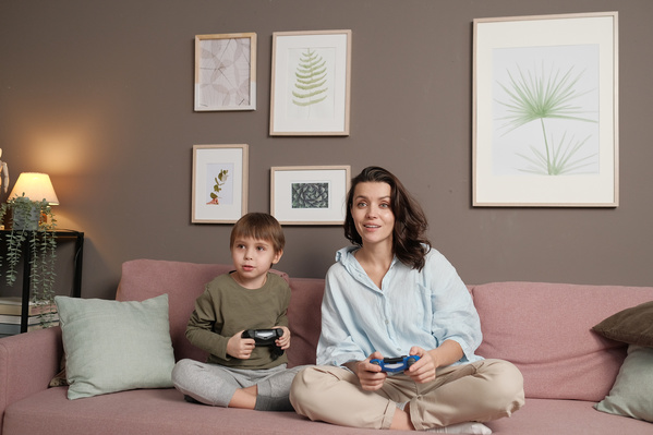 A woman in a light shirt and her little son in pajamas playing video games with joysticks