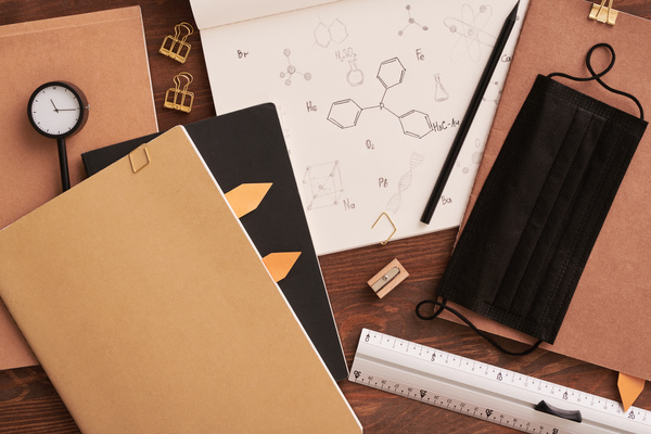 Notes on chemistry in a notepad and classy brown stationery lying on a wooden table with a black medical mask