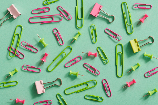 Top view of pink and green stationery for attaching papers laid out on a turquoise background