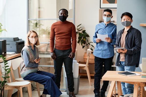 Colleagues dressed in strict clothes and reusable medical masks being in a bright office