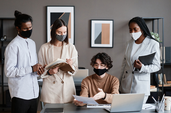 Office workers in strict clothes and with reusable medical masks on their faces in a modern office discussing a document