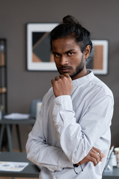 Portrait of a male employee with black gathered hair and an earring in his nose wearing a white shirt posing in the office