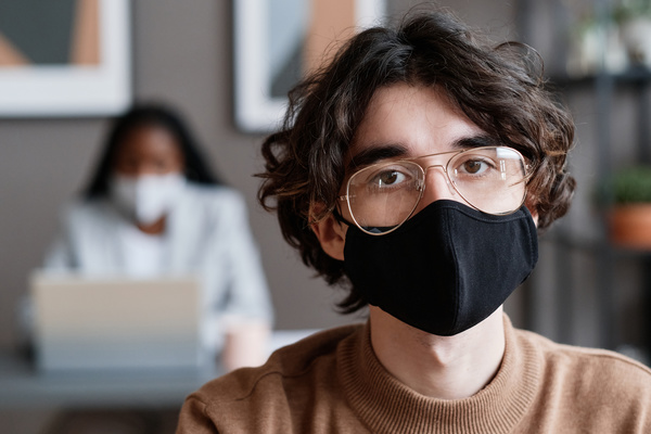 Portrait of an male employee with dark curly hair wearing a black face mask in the office