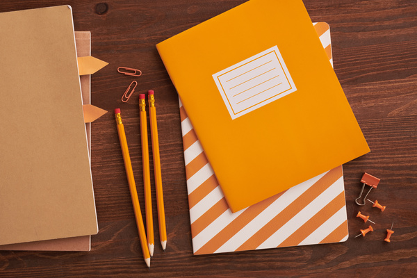 Orange notebooks lying with graphite pencils and paper office supplies on a wooden table