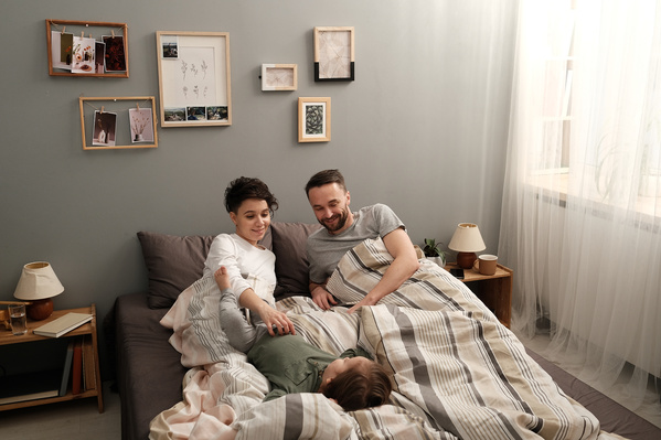Smiling parents in pajamas lying in bed with their little son in a green longsleeve