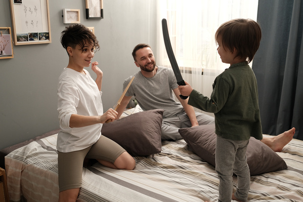 A woman in pajamas playing sword fighting with her little son on the bed
