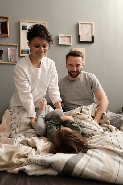 Laughing parents in pajamas having fun with their little son in a green longsleeve in bed