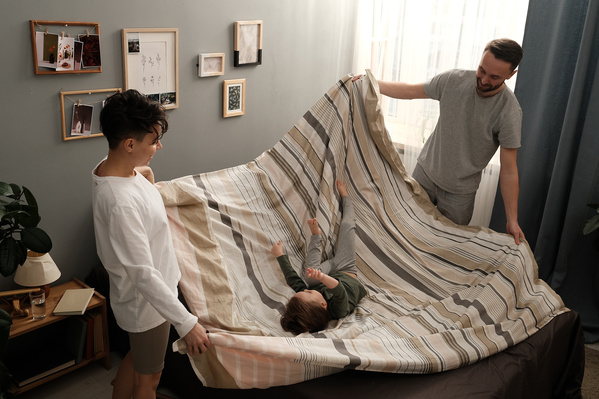 Mom with short hair and dark-haired father in pajamas fooling around with their little son on the bed