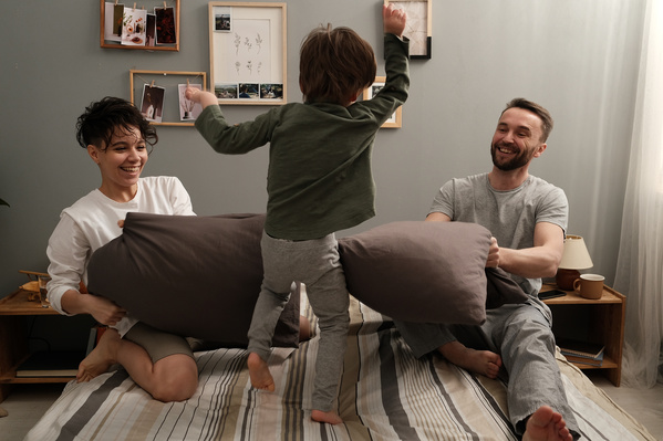 Parents in pajamas and their little son playing pillow fight on the bed at home
