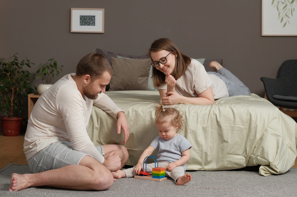 A family consisting of brown-haired parents and their little daughter playing with wooden toys in a bright bedroom