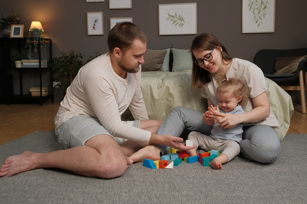 Mom and dad in light pajamas playing with their little blonde daughter with colorful wooden blocks