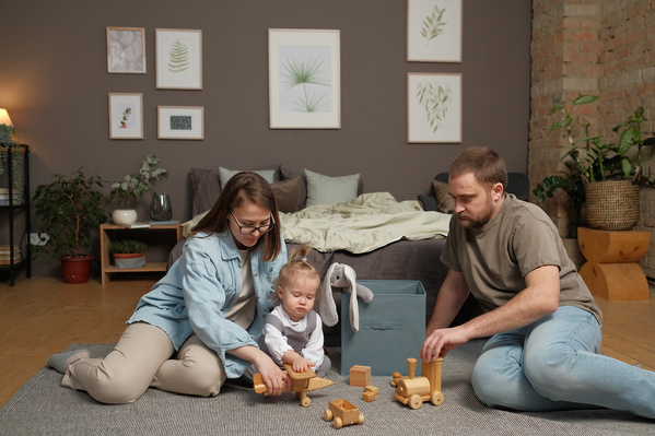 Mother and father in light pajamas playing with their little blonde daughter with colorful wooden toys