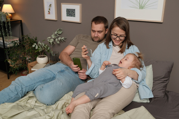 A family consisting of parents and their son looking at the phone screen while sitting in bed
