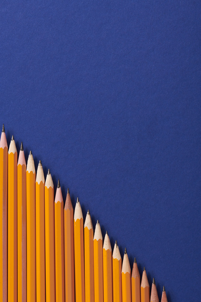 Yellow graphite pencils arranged in descending order on a dark blue surface